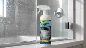 Mommy’s Glass hard water spot remover on a shower ledge beside cloudy and clear glass